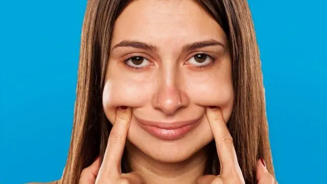 Una mujer forzándose una sonrisa con las manos.