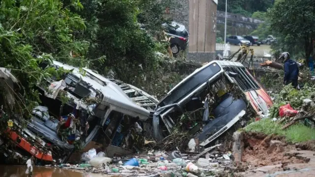 A man observes damaged public buses at a river after pouring rains in Petropolis, Brazil. Photo: 16 February 2022