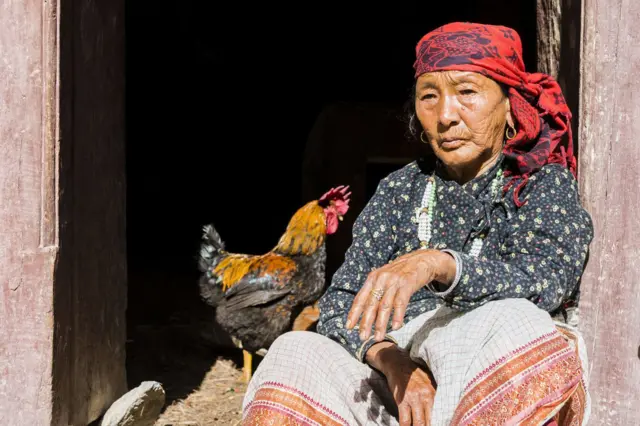 म्याग्दीमा कुखुराको छेउमा एक वृद्धा