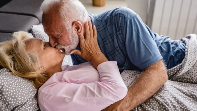 Idosos se beijando deitados numa cama