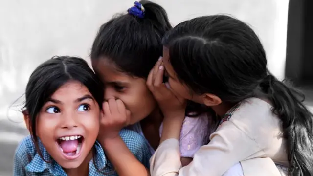 Three girls talking into each other's ears