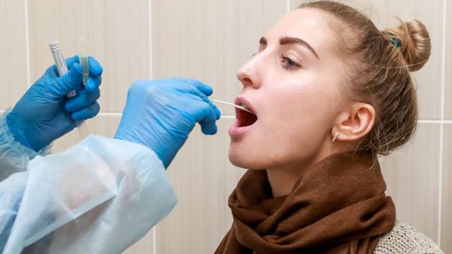医护人员正用拭子探入该年轻女性喉咙后部提取检测样本