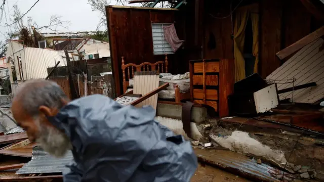 Hombre pasa por delante de una casa destruida en Puerto Rico.