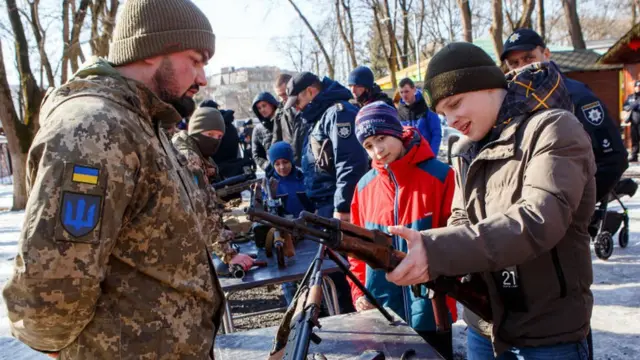 Ukrainian soldiers and civilians inspect weapons during a defence drill