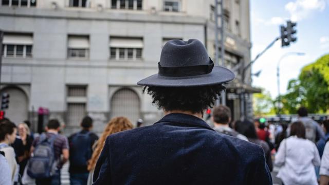 A man wearing a hat with his back to camera crosses a road