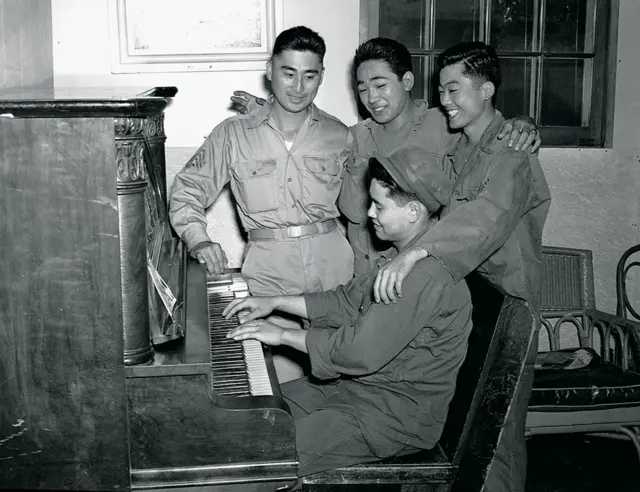A soldier plays an piano as soldiers sing along