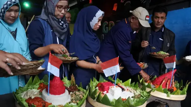 Warga memotong tumpeng Merah Putih saat menyambut Hari Kemerdekaan Indonesia di sebuah kafe di Desa Talkandang, Situbondo, Jawa Timur, Kamis (16/08).