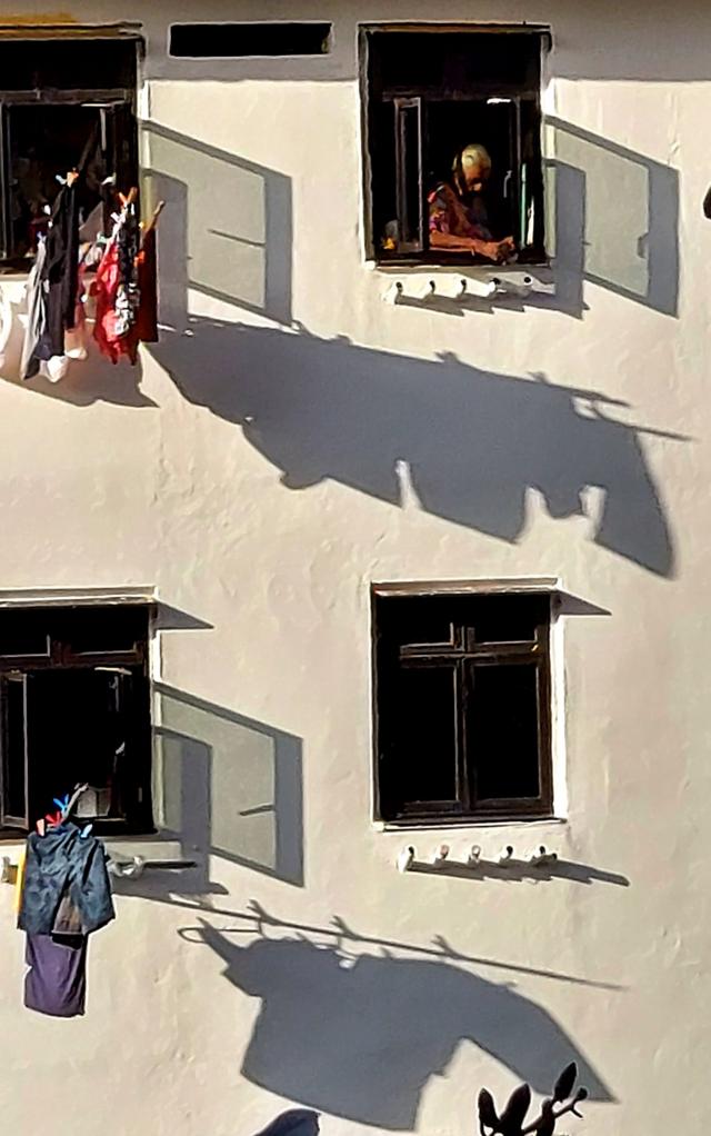 Một cụ bà đang chuẩn bị phơi quần áo bên ngoài ô cửa sổ một khu căn hộ cũ được bảo tồn tại Bukit Merah.