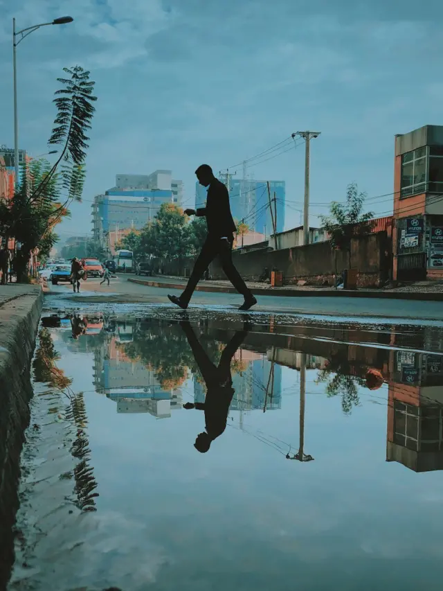 አንድ መንገደኛ ዉሃ ባቆረ መንገድ ሲሻገር የሚያሳይ ፎቶግራፍ።