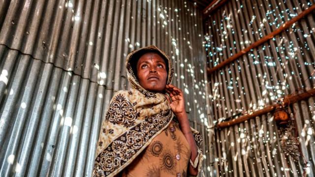 امرأة تنظر إلى الضوء المتسلل إلى بيتها من الثقوب التي أحدثها القصف للمجمع السكني الذي تعيش فيه في مدينة "هوميرا" بإقليم تيغراي.