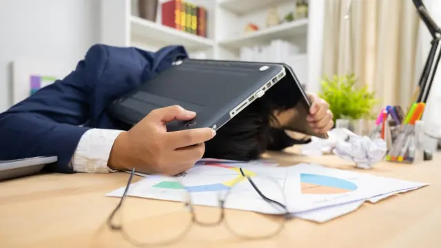 Una persona abrumada con la laptop cubriéndole la cabeza