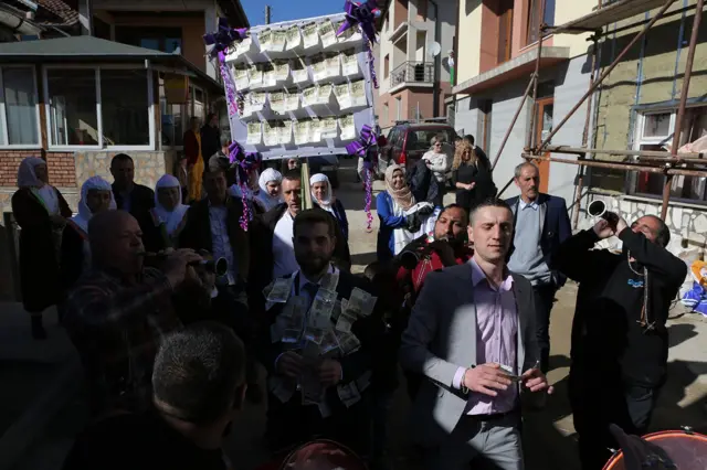 Povorka, praćena zvucima tupana i zurli, polako se kreće prema trgu u centru sela. Uobičajena praksa je da se novac dobijen od rodbine i prijatelja javno „izlaže“ na posebnim, za tu svrhu izrađenim panelima.