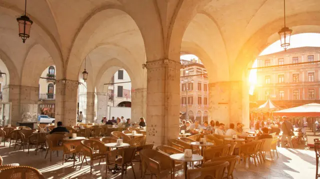 Șiruri de mese, în lumina apusului, sub o arcadă impunătoare în centrul istoric al orașului Treviso din Italia