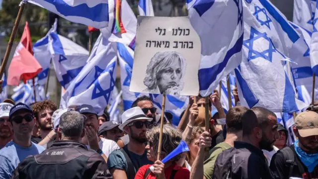 Manifestantes portan banderas israelíes y un cartel que dice "Todos somos Gali Baharav-Miara" durante una manifestación contra la reforma judicial.