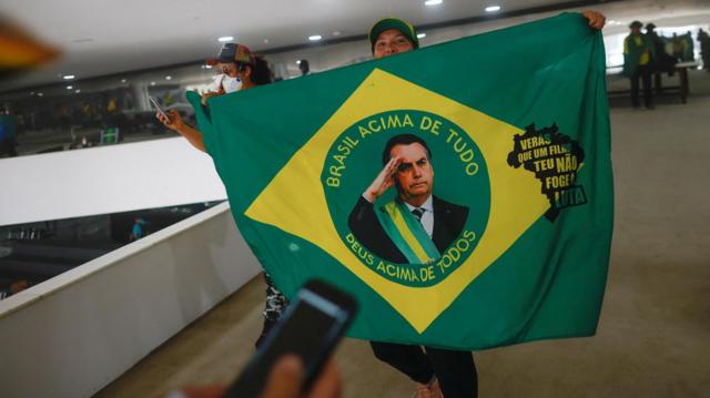 Mulher segura bandeira com rostoplataformas de apostas desportivasBolsonaro dentro do Planalto invadido