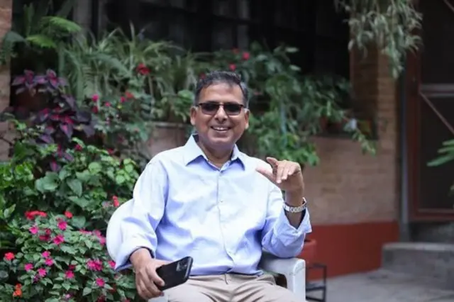 घरबाहिरको बगैँचामा सेतो कुर्सीमा बसिरहेका संविधानविद् विपिन अधिकारी