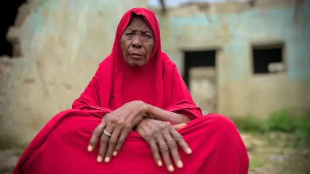 Maryam Jidda ree, o jokoo, o ka ọwọ rẹ mejeeji sori ara wọn pẹlu aṣọ pupa to wọ, o n wo orere.