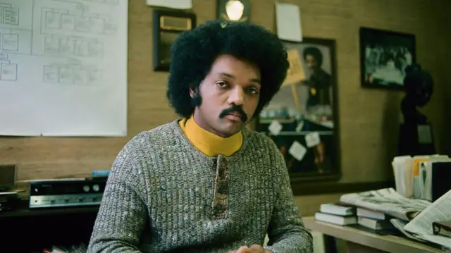 Jesse Jackson en los inicios de su carrera.  Está sentado en una oficina mirando directamente a la cámara.