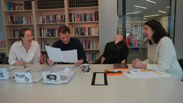 Три жінки та чоловік сидять за столом у редакції і сміються