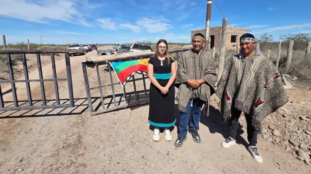 Três pessoas de pé em frente a uma porteira