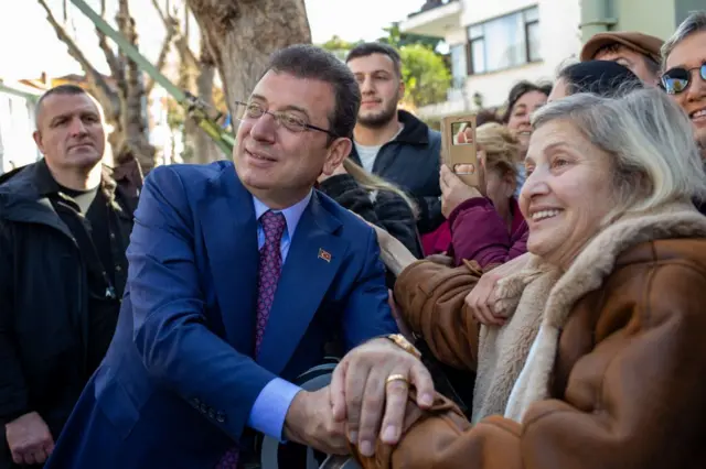 İmamoğlu, 9 Mart 2025'te Adalar sakinleriyle. Adalar'daki bir yaşlı kadının elini tutup fotoğraf çektiriyor. 