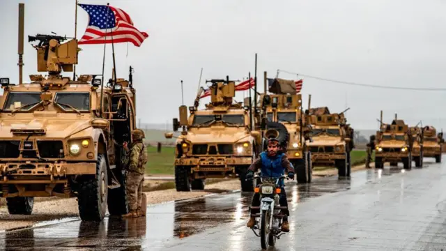 Tanklar, üzerlerinde Amerikan bayrakları var, önde motorsikletli bir Suriyeli