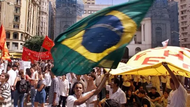 Protesto na rua com pessoa levantando bandeira do Brasil