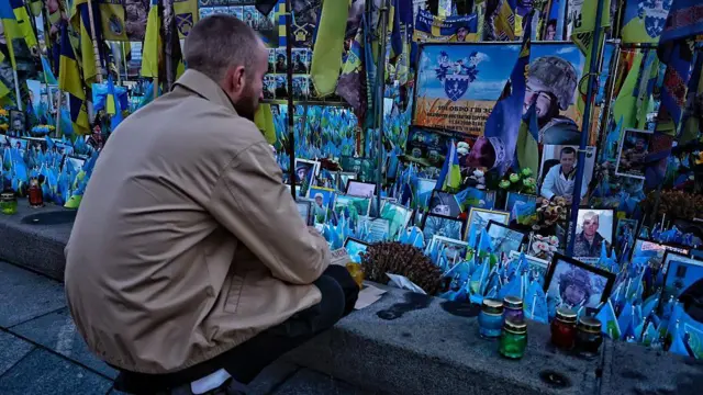 Чоловік присів біля імпровізованого меморіалу загиблим українським воїнам та іноземним добровольцям на Майдані Незалежності 