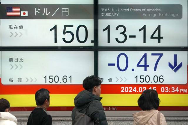 Japoneses pasan frente a una pantalla mostrando la cotización de yen frente al dólar. 