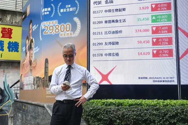 Un hombre en Hong Kong consulta su teléfono móvil frente a una valla que anuncia los datos de la bolsa de valores