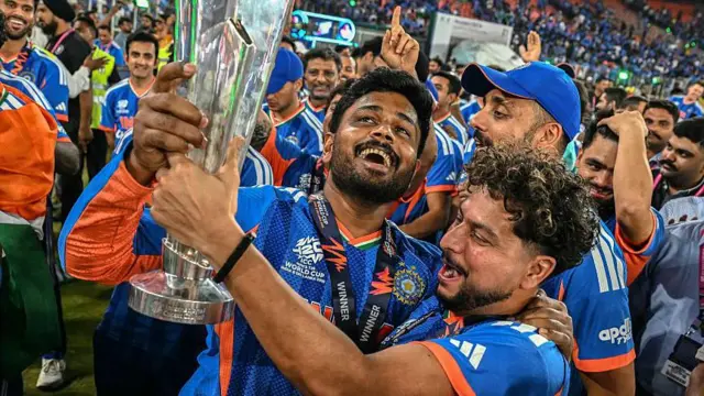 8 मार्च 2026 को अहमदाबाद के नरेंद्र मोदी स्टेडियम में न्यूज़ीलैंड के ख़िलाफ़ 2026 ICC मेन्स T20 क्रिकेट वर्ल्ड कप का फ़ाइनल मैच जीतने के बाद, भारत के संजू सैमसन (बीच में) और कुलदीप यादव (बीच में, दाईं ओर) जीत का जश्न मनाते हुए ट्रॉफी के साथ.