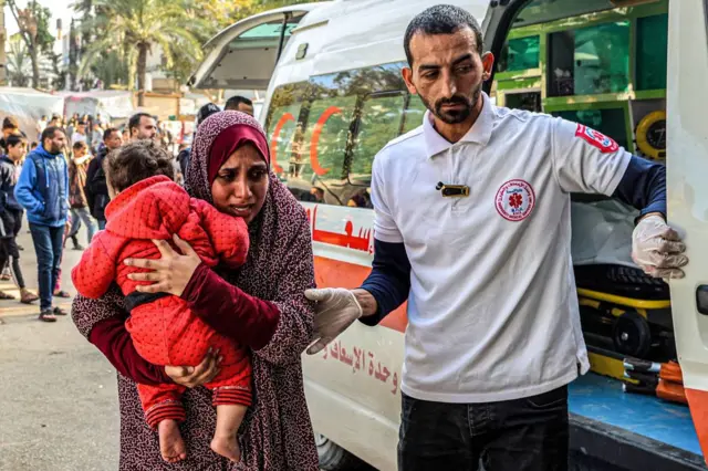 A paramedic assists a woman carrying a child arriving at the European Hospital in Khan Yunis in the southern Gaza Strip on December 31, 2023,