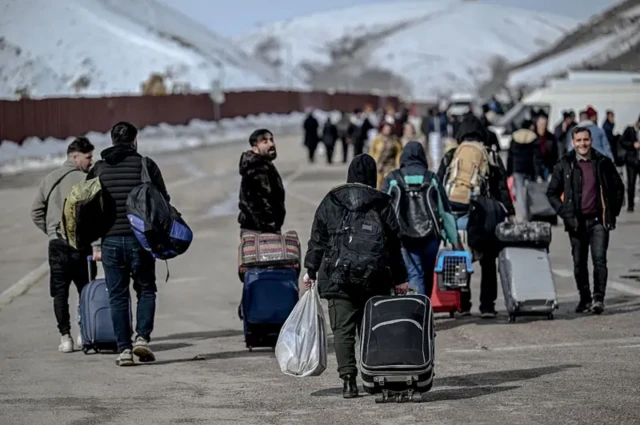 تعدادی چمدان به دست در گذرگاه مرزی در حال راه رفتن هستند