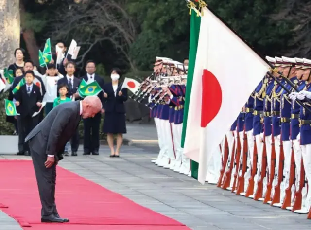 Lula se curvando em direção a bandeiras do Japão e Brasil, durante cerimônia