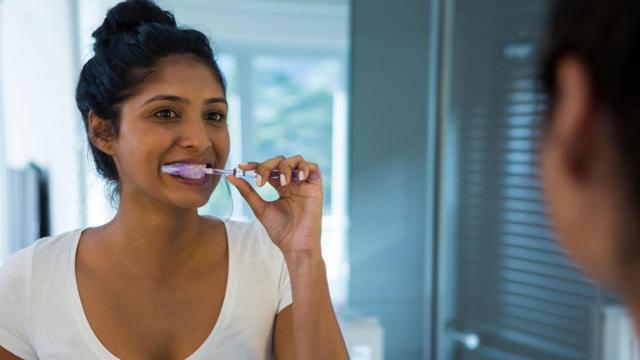 Una mujer cepillándose los dientes frente al espejo