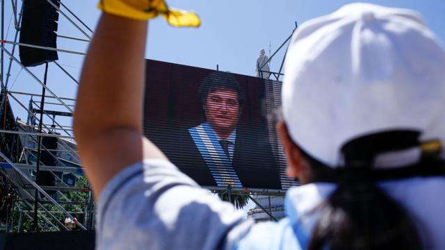 Foto colorida mostra apoiador(a)casa da dona bet365Milei com camiseta da argentina,casa da dona bet365costas,casa da dona bet365frente a um telão com fotocasa da dona bet365Milei tomando posse