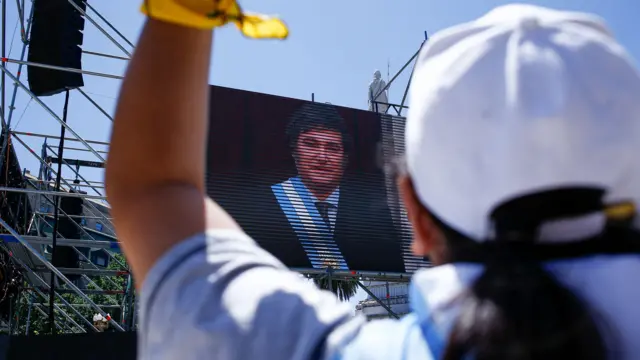 Foto colorida mostra apoiador(a)suporte sporting betMilei com camiseta da argentina,suporte sporting betcostas,suporte sporting betfrente a um telão com fotosuporte sporting betMilei tomando posse