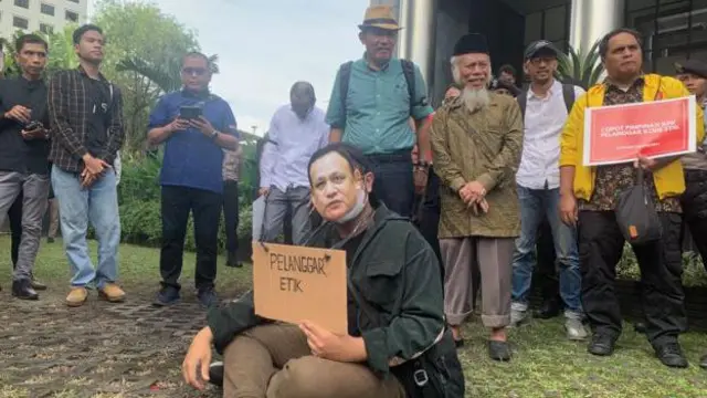 Seorang pengunjuk rasa duduk dengan mengenakan topeng Ketua KPK Firli Bahuri dan karton bertulisan “Pelanggar Etik“ pada aksi unjuk rasa depan Gedung KPK, Senin (10/4).