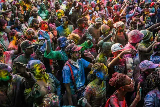 Crowds of dancing people are covered in multicoloured powder.