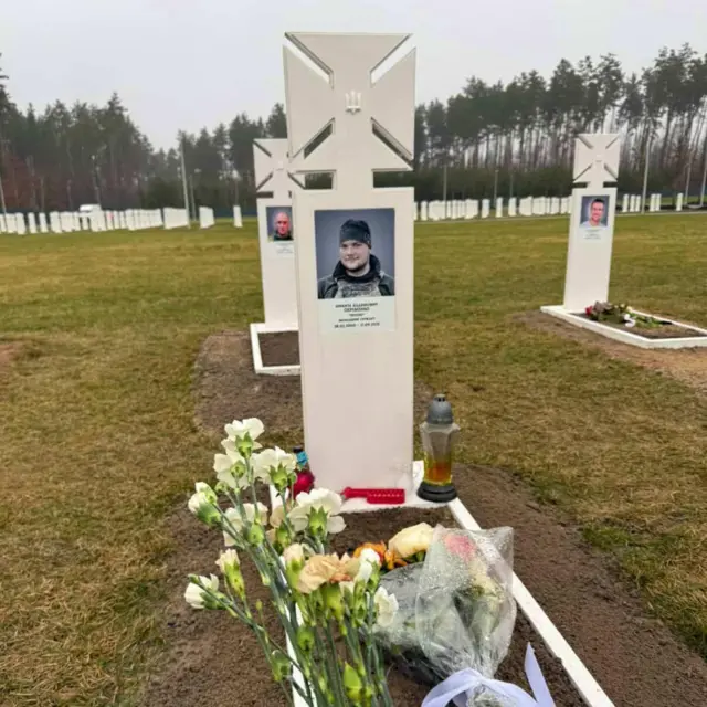 Могила військового з кам'яним хрестом білого кольору, на могилі лежать квіти