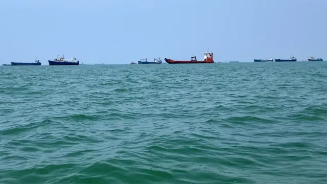 海上有至少十艘大型船隻。海面有些波濤起伏，天空湛藍。