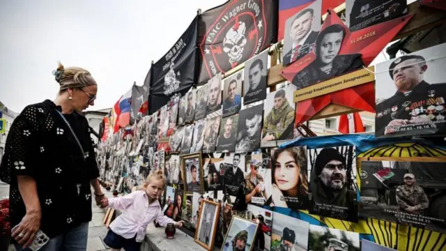 Mulher,palpites esporte betmão dada a uma menina, observa mural com fotospalpites esporte betcombatentes