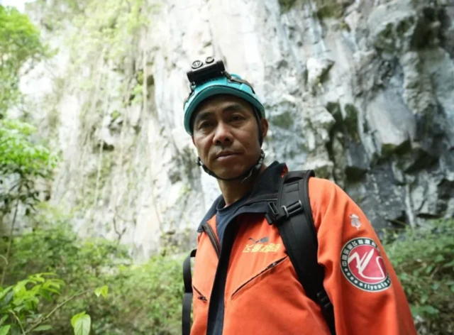 Homem com agasalho vermelho, com capacete e uma mochila