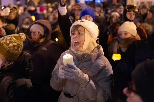 Personas asisten a una vigilia con velas organizada por personal sanitario en el lugar donde Alex Pretti fue asesinado el 24 de enero de 2026 en Minneapolis, Minnesota. Van vestidas con mucha ropa de abrigo: chaqueta, guantes grandes, pasamontañas, gorros. Llevan velas en sus manos. 