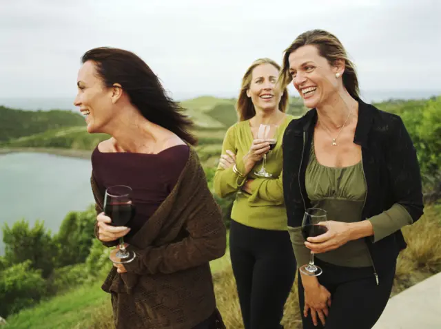 Three women hold glasses of wine for outside