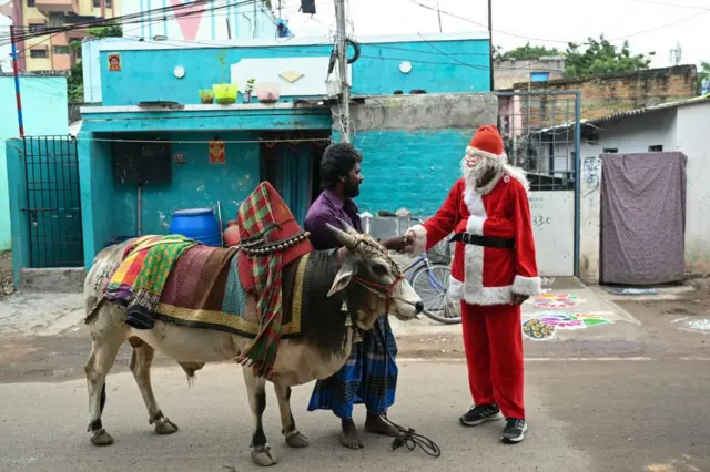A man dressed in Santa Claus outfit greets a man along the lanes of a residential cluster ahead of Christmas in Chennai, on December 24, 2024. 