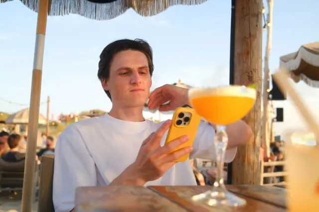 Joven con un trago a un costado y el celular en la mano