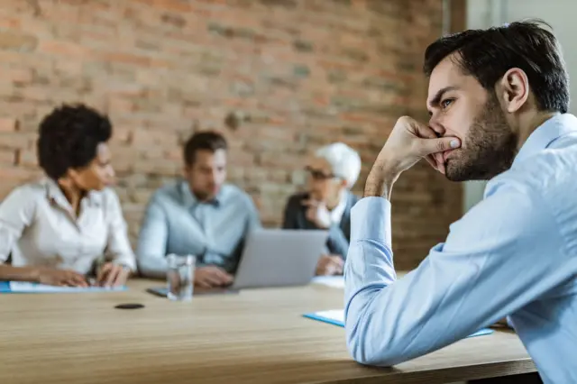 Homem com semblante de preocupação durante reunião de trabalho.