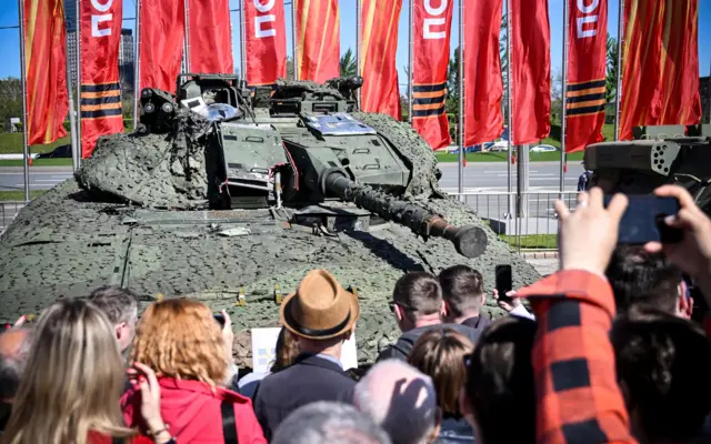 2024年5月1日,游客在莫斯科的波克隆纳山二战纪念园区观看一辆瑞典 CV 940 型装甲运兵车,该车由俄罗斯军队在乌克兰缴获并展出。俄罗斯国防部开设了“西方武器与军事装备”样品展览,展示俄军在乌克兰夺取的装备。这辆车呈绿色,覆盖伪装网,炮塔指向人群