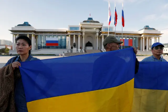 Três pessoas segurando a bandeira da Ucrânia do ladojogos virtuais pixbetfora do palácio do governo da Mongólia.